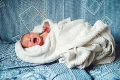 crying-newborn-baby-lying-on-a-sofa-covered-by-a-5YPDWN8.jpg