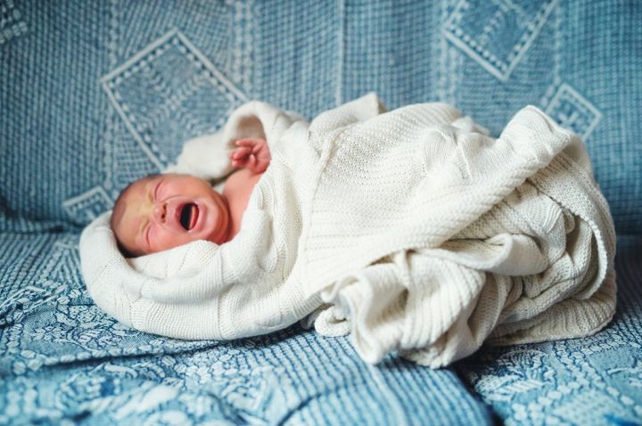crying-newborn-baby-lying-on-a-sofa-covered-by-a-5YPDWN8.jpg