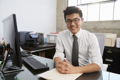 young-asian-male-professional-at-desk-smiling-to-RU9HW36-e1564404185192.jpg